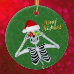 Alberner Weihnachtseleton-Hut Ornamente Grün<br><div class="desc">Dieses hängende Keramik-Ornament hat ein albernes Skelett, das rote und grüne Ornamente an seinen Augen hält, während er lächelt und einen aus Pelz getrimmten roten Weihnachtsmann trägt, der auf einem grünen Hintergrund mit Imitaten goldglänzenden Flecken aus Gold steht. Fröhlicher Weihnachtstext in Gold auf der Vorderseite. Passen Sie Ihren Text auf...</div>