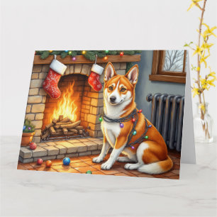 Basenji sitzt neben dem Kamin mit Weihnachtsbeleuc Karte