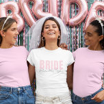 Bride T - Shirt | Personalisiert Future Frau Name<br><div class="desc">Dieser moderne und personalisierte Bride T - Shirt ist das perfekte Outfit für jede zukünftige Braut! Mit sanft blütenrosa "BRIDE" Text gepaart mit eleganter handgeschriebener "Future Mrs. [Ihr Name]", ist dieses Tee ideal für Brautpartys, Junggeselinnen-Abschiede, Hochzeitsfeiern und Flitterwochen. Erhältlich in verschiedenen Stilen und passt für den Komfort und das Aussehen...</div>