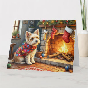 Cairn Terrier sitzt vor dem Kamin mit Weihnachtsbe Karte