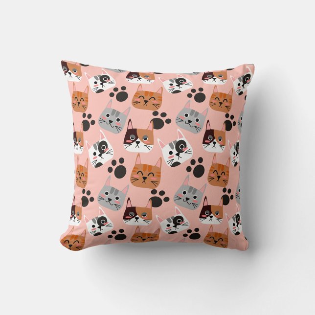 Cat Faces Kissen (A flat lay shot shows a square pillow with a pink background and a repeating pattern of cartoon cat.)