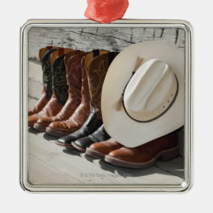 Cowboyhut auf Reihe der Cowboystiefel außerhalb Silbernes Ornament