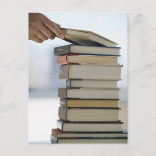 Die Hand des Mannes, die ein Buch von einem Stapel Postkarte