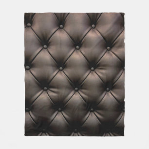 Ein dunkles Lederkissen als Hintergrund, von einem Fleecedecke