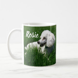 Ein weißes Poodle, das sich in üppig grünem Gras r Kaffeetasse