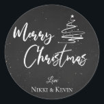 Elegant Chalkboard Script Merry Christmas Tree Runder Aufkleber<br><div class="desc">Elegantes Chalkboard Script Frohe Weihnachtsbaum Classic Round Sticker. Passen Sie es an,  indem Sie die Namen ändern. Das Design hat frohe Weihnachten geschrieben in hübschem Schriftart auf einem Kreideboden zusammen mit den Namen des Paares. Für weitere Anpassungen wenden Sie sich bitte an mich unter mypaperlove2021@gmail.com</div>