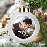 Erste Weihnachts Verlobte benutzerdefinierte Foto  Keramik Kugel-Ornament<br><div class="desc">Gedenken Sie Ihre Verlobung mit diesem schönen modernen Sakraldekor. Der weiße Text lautet "Unser erstes Weihnachtsfest verlobt", mit dem Wort "verlobt" in eleganter Kalligraphie-Schrift mit dekorativen Swashes vor und danach. Ersetzen Sie das Beispielbild durch Ihr Lieblings-Foto, und fügen Sie Ihre Namen und das Jahr hinzu. Ein Filter mit schwarzem Farbverlauf...</div>