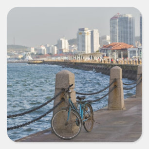 Fahrrad am Wasser mit der Skyline von Yantai Quadratischer Aufkleber