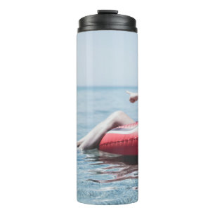 Frau auf einem aufblasbaren Schwimmer im Ozean, de Thermosbecher