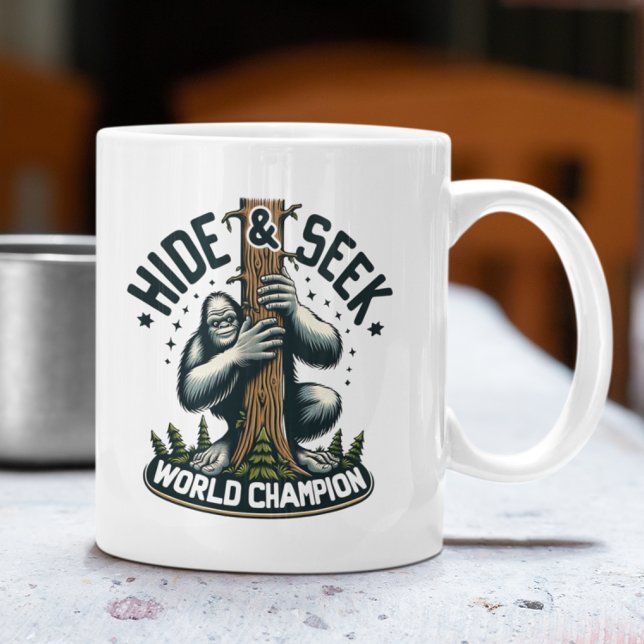 Funny Hide & Seek Weltmeister Bigfoot Kaffeetasse (White mug with Bigfoot "Hide & Seek World Champion" design on an outdoor table.)