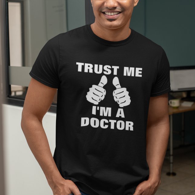 Funny Trust Me Ich bin Arzt T-Shirt (Man wearing a black "Trust Me, I'm A Doctor" t-shirt with thumbs-up graphic.)