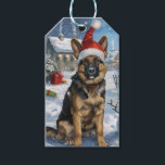 German Shepherd Winter Wonderland Christmas Joy Geschenkanhänger<br><div class="desc">Dieses festliche Design spiegelt den fröhlichen Geist der Urlaubssaison wider und besticht durch ein hübsches Jungtier mit einer Weihnachtsmannmütze. Der Hund ist eingebettet in ein winterliches Wunderland, mit einem Schneemann, einem dekorierten Weihnachtsbaum und wunderschön verpackten Geschenken. Schneeflocken fallen sanft ab und geben der Szene eine magische Touch, während die lebhaften...</div>