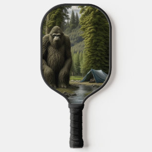 Grosser Bigfoot sitzend neben Zelt im Wald Pickleball Schläger