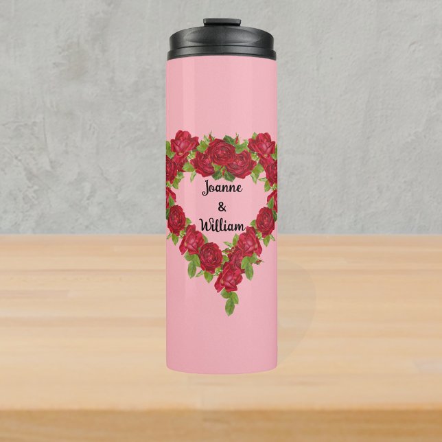Herzförmiger Kranz von rote Rosen auf hellrosa Thermosbecher (Romantic heart shaped wreath of red roses and leaves on light pink thermal drink bottle.)