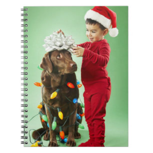 Junger Junge, der Weihnachtslichter um einen Hund Notizblock