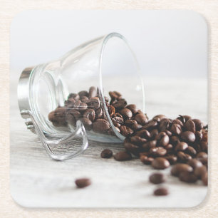 Kaffeebohnen, die sich aus einem klaren Kaffeecup Rechteckiger Pappuntersetzer