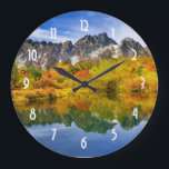 Landschaftliche Landschaftswälder und Berge Große Wanduhr<br><div class="desc">Eine Uhr mit einem schönen Landfoto. Steinberge mit einem Herbstwald in lebhaften Farben. Ein ruhiger See reflektiert die Berge,  Bäume und Gräser.</div>