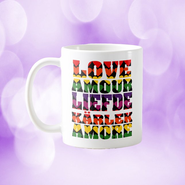Liebe in vielen Sprachen Dunkler Regenbogen Kaffeetasse (A mug that says love in a variety of languages with rainbow hearts.)