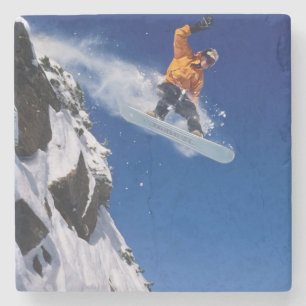 Mann auf einem Snowboard, der von einem Gesims spr Steinuntersetzer