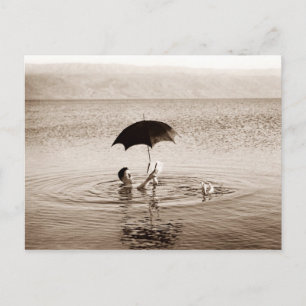 Mann liest unter einem Regenschirm im Toten Meer Postkarte