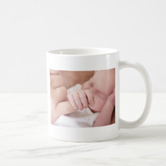 neugeborenes Baby, das Vaterfinger hält Tasse