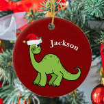 Niedlich Dinosaurier Weihnachten Keramik Ornament<br><div class="desc">Phantastischer grüner Dinosaurier lächelt und sieht sehr niedlich in einem Urlaub roten Weihnachtsmannmütze. Ich mag prähistorische Weihnachtstiere und Geschenke,  die Kinder Liebe. Passen Sie dieses Geschenk mit dem Namen des Empfängers an,  um es noch personalisierter zu machen.</div>