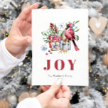 Niedliche Aquarellfarbe Kardinal Bird Weihnachtska Feiertagspostkarte<br><div class="desc">Diese gemütliche Urlaubspostkarte zeigt eine Aquarellbilder eines roten Kardinals, der auf einer Ansammlung geschenkter Weihnachtsgeschenke steht und von heiligen und mistletosen Grünpflanzen und stilisierten blauen Schneeflocken umgeben ist. Das Wort "JOY" erscheint in großen, abgestuften roten Serifenbriefen, die sich mit der Kunst abstimmen. Fügen Sie den Namen Ihrer Familie und das...</div>
