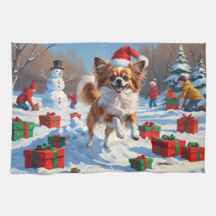Papillon-Hund läuft im Schnee mit Weihnachtsmütze Geschirrtuch