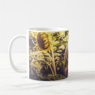 Person mit weißem Hut neben Sonnenblumenfeldern Kaffeetasse