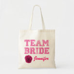 Pink Team Bride Tote Bag Tragetasche<br><div class="desc">Spaß Hochzeitsfeier Leinwand Tasche mit rosa Grafik Not Text lesen Team Bride. Benutzerdefinierter rosa Skripttext am unteren Rand ist bereit, für das gesamte Brautparty zu personalisieren. Die digitale Grafik einer rosa Rosenblüte schmückt den Boden links. Ideal, um alle wichtigen Dinge zu halten, die die Mitglieder des Brautparty nicht vergessen können....</div>