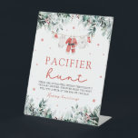 Red Christmas Santa Baby Schnuller Hunt Kinderdusc Sockelschild<br><div class="desc">Das Red Christmas Santa Baby Schnuller Hunt Baby Shower Game Sign verleiht Ihrer Babydusche eine Touch von Urlaubsspass und Spannung. Dieses Schild mit weißem Hintergrund mit festlichen roten Schneeflocken, fröhlichen roten Beeren, winterlicher Eukalyptusgrün und Babykleidung im Weihnachtsstil lädt die Gäste zum Schnuller Hunt ein. Die Gäste können in der Umgebung...</div>