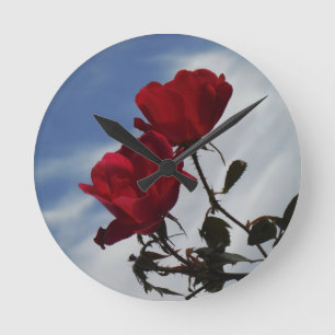 Rote Rosen gegen einen hellen blauen Himmel Runde Wanduhr