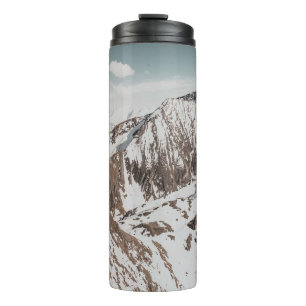 SCHNEEBEDECKTER BERG UNTER WEISSEN WOLKEN WÄHREND THERMOSBECHER