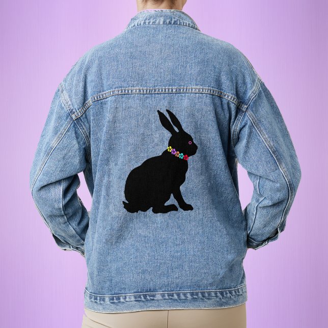Schwarze Silhouette-Kaninchen-Blume mit seitlichem Jeansjacke (Sitting black silhouette bunny rabbit with ring of colourful flower petals on a womans denim jacket.)