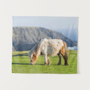 Shetlandpony auf Weide in der Nähe hoher Klippen Wandteppich