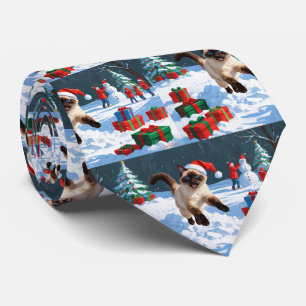 Siamische Katze läuft im Schnee mit Weihnachtsmütz Krawatte