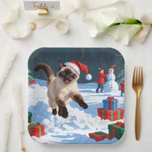 Siamkatze läuft im Schnee mit Weihnachtsmütze Pappteller
