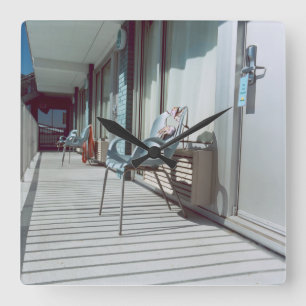 Stühle außerhalb der Strand-Hotelzimmer Quadratische Wanduhr