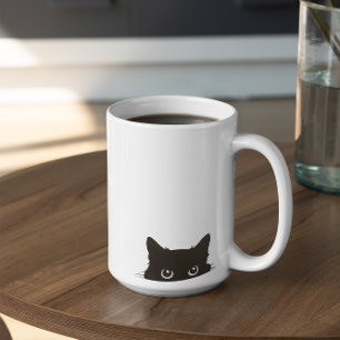 Süße spähende schwarze Katze, die mit großen Augen Tasse
