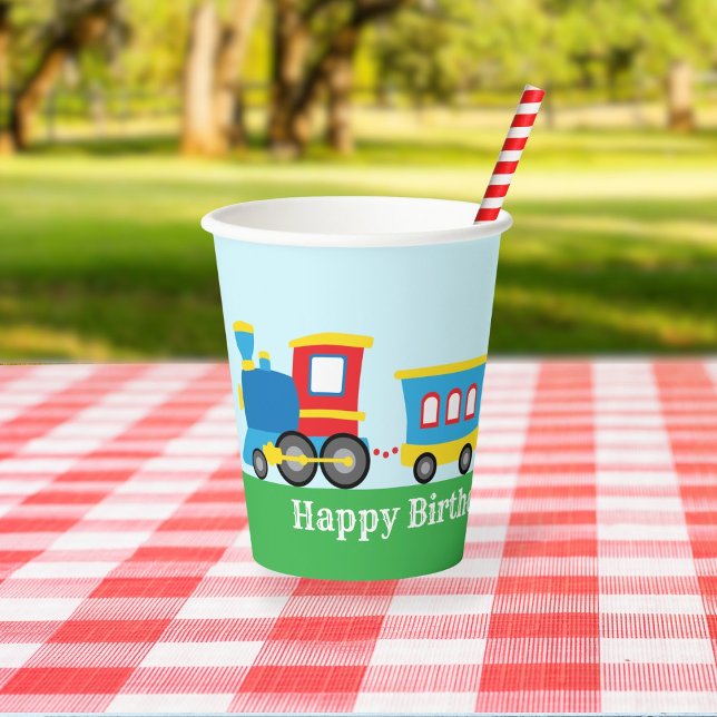 Süße Zug-Geburtstagsfeier Pappbecher (A paper cup decorated with a cute cartoon train sits on a picnic table in a park.)