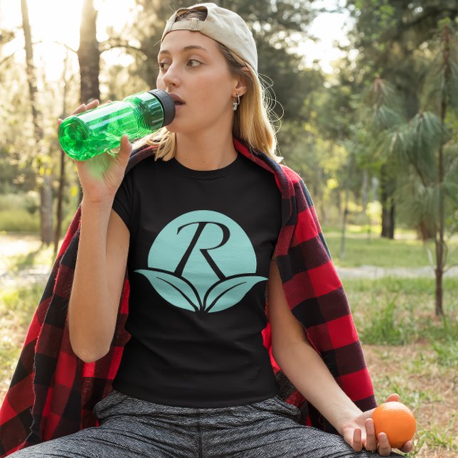 Symbol für Jugendliche - Körperpflege T-Shirt (Young woman wears a black shirt with the Rejuvenescents "R" leaf logo. She sips water, holds orange.)