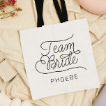 Team Bride Modern Script Gold Wedding Name Tragetasche<br><div class="desc">Diese moderne Tasche mit minimalistisch lässigem, schicken Skript-Kalligraphie-Design, TEAM BRIDE-Lektüre sowie der individuelle Name Ihrer Trauzeugin oder Brautjungfrau verfügt über klare Linien, um ein schlankes und raffiniertes Aussehen zu schaffen. Der schlichte Stil mit den kleinen, bedruckten Details des Goldenen Herzens verleiht ihrem Hochzeitslook eine Touch Raffinesse. Auch ein tolles Brautparty...</div>