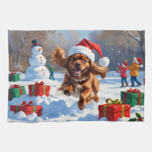 Tibetischer Spaniel läuft im Schnee mit Weihnachts Geschirrtuch