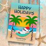 Tropical Beach Santa Hammock Weihnachten<br><div class="desc">Die Weihnachtskarte zum Thema Tropical und Küstenweihnachtszeit lädt zum Entspannen in einer Hängematte am Strand ein. Hier genießen Sie die Meereswellen und den bunten Sonnenuntergang und die festlichen Palmen, die in Strandlichter verziert sind. Der obere Gruß sagt "Happy Holidays" in marineblau. Der Gruß im Sand und der Name können personalisiert...</div>