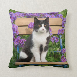 Tuxedo Katze sitzt auf einem Gartenstuhl mit Blume Kissen