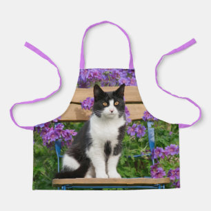 Tuxedo Katze sitzt auf einem Gartenstuhl mit Blume Schürze