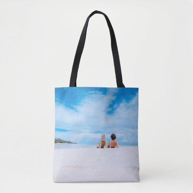 Two women lying on white sand facing beach under b (Vorderseite)