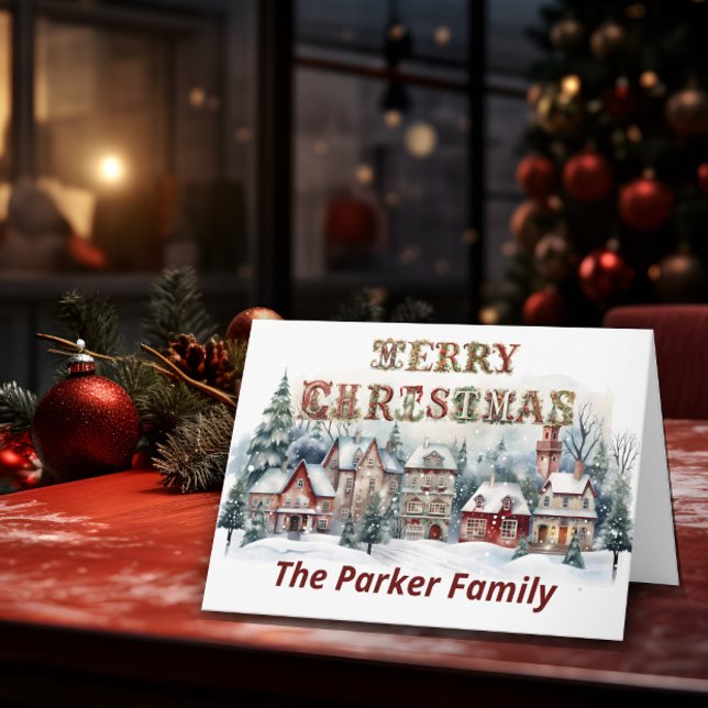 Viktorianisches Dorf Frohe Weihnachten Karte (A Christmas card stands on top of a table with Christmas elements in the background.)