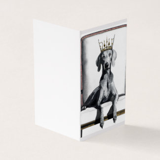 Weimaraner mit einer Krone auf einem Stuhl sitzend