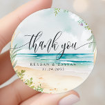 Wir danken Ihnen für die Hochzeit von Watercolor B Runder Aufkleber<br><div class="desc">Watercolor Beach Wedding danke Ihnen klassische Round Sticker. Dieses Design besticht durch eine wunderschöne Aquarellsommerstrandszene. In diesem tropischen Design sind Meereswellen,  Sand und Blume zu finden.</div>